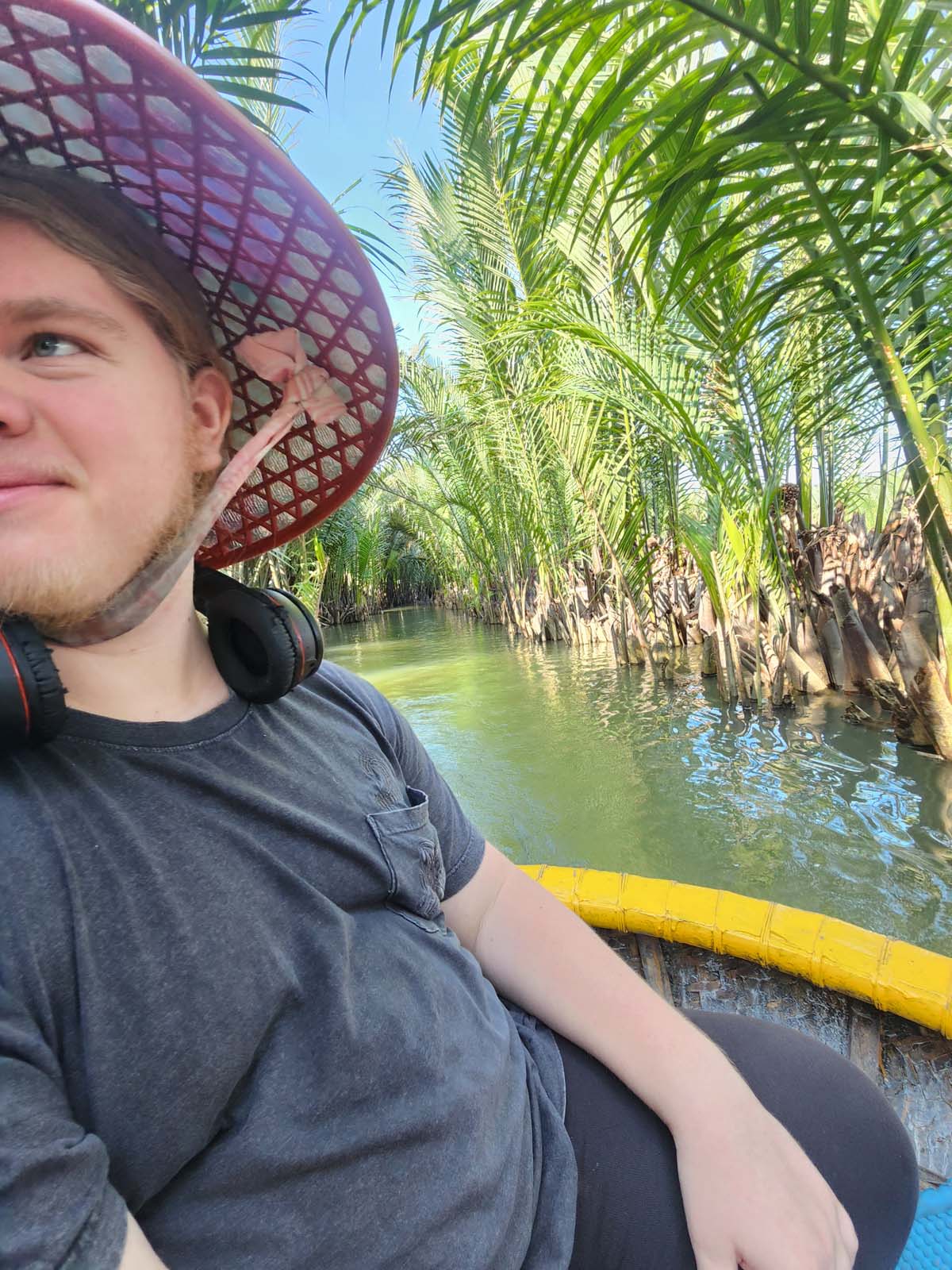Damian's little brother Ian wearing a sun hat on a bowl-shaped boat surrounded by palm trees.