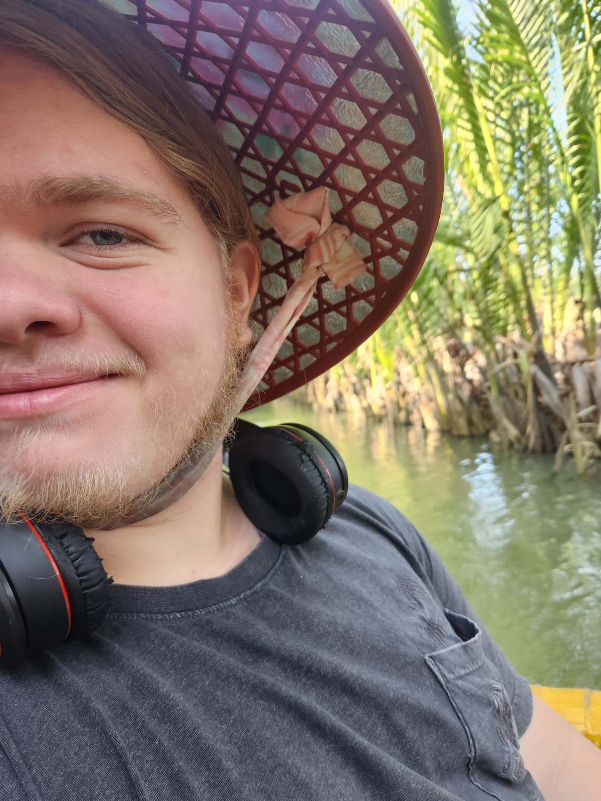 Photo of ian wearing a sun hat smiling at the camera from a coconut boat in a palm forest.