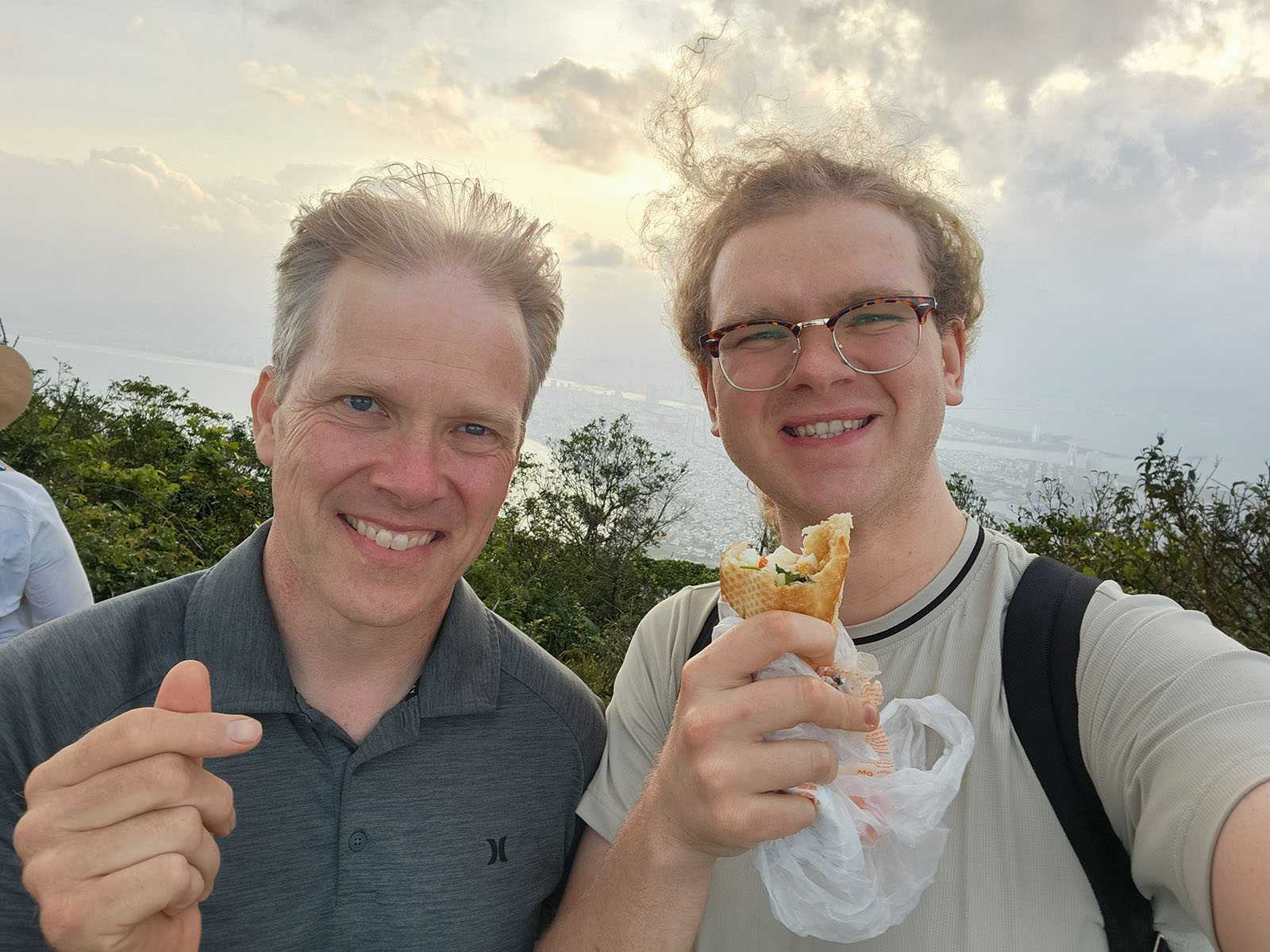 Damian holding a banh mi and Uncle Tim making a heart with his fingers on top of Monkey Mountain.