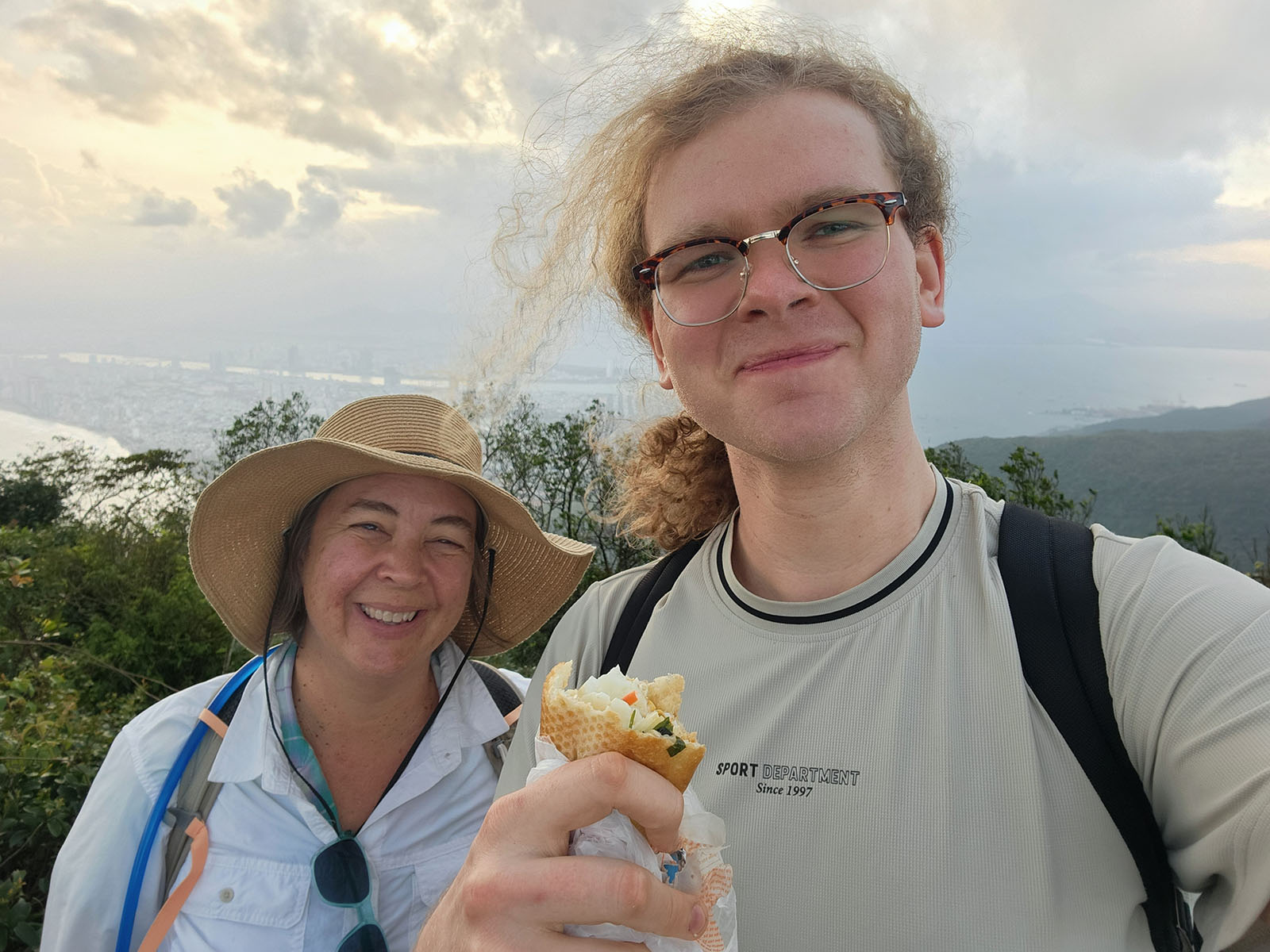 Damian and Janet smiling with a vegetarian banh mi on top of Monkey Mountain.