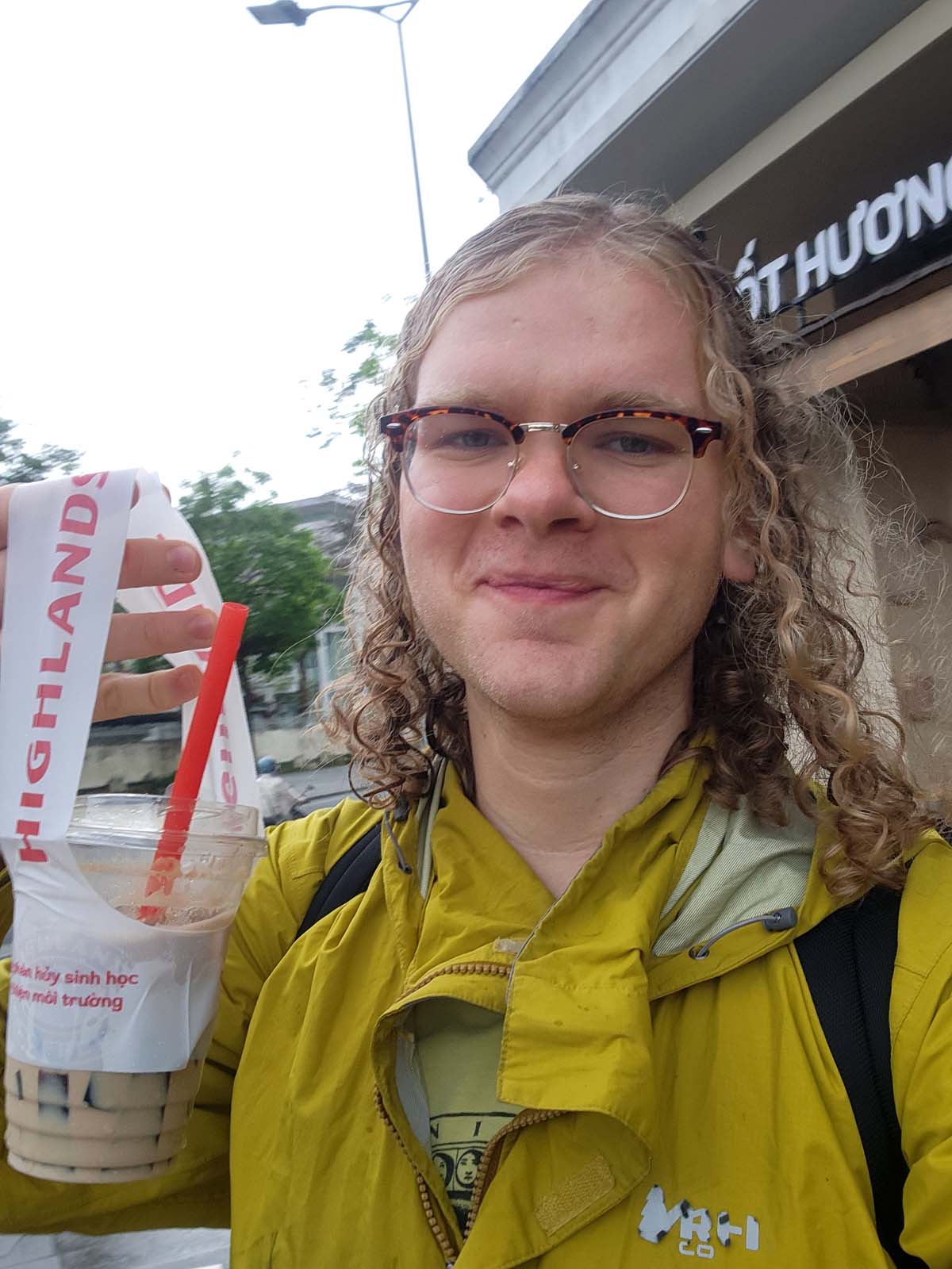 A selfie of Damian smiling with wet hair while holding an iced coffee.