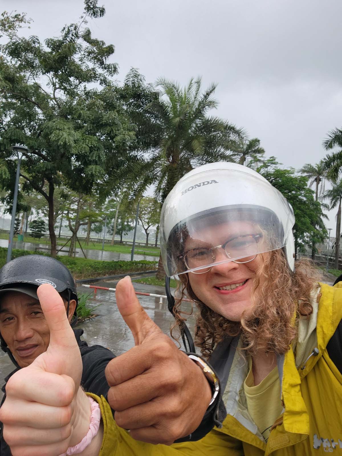 A selfie of Damian smiling in a motorbike helmet, holding out thumbs up with driver Xanh.