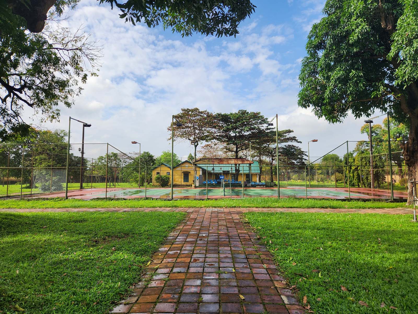 Ceramic tile path leading to a Western-style tennis court surrounded by chain link fence.