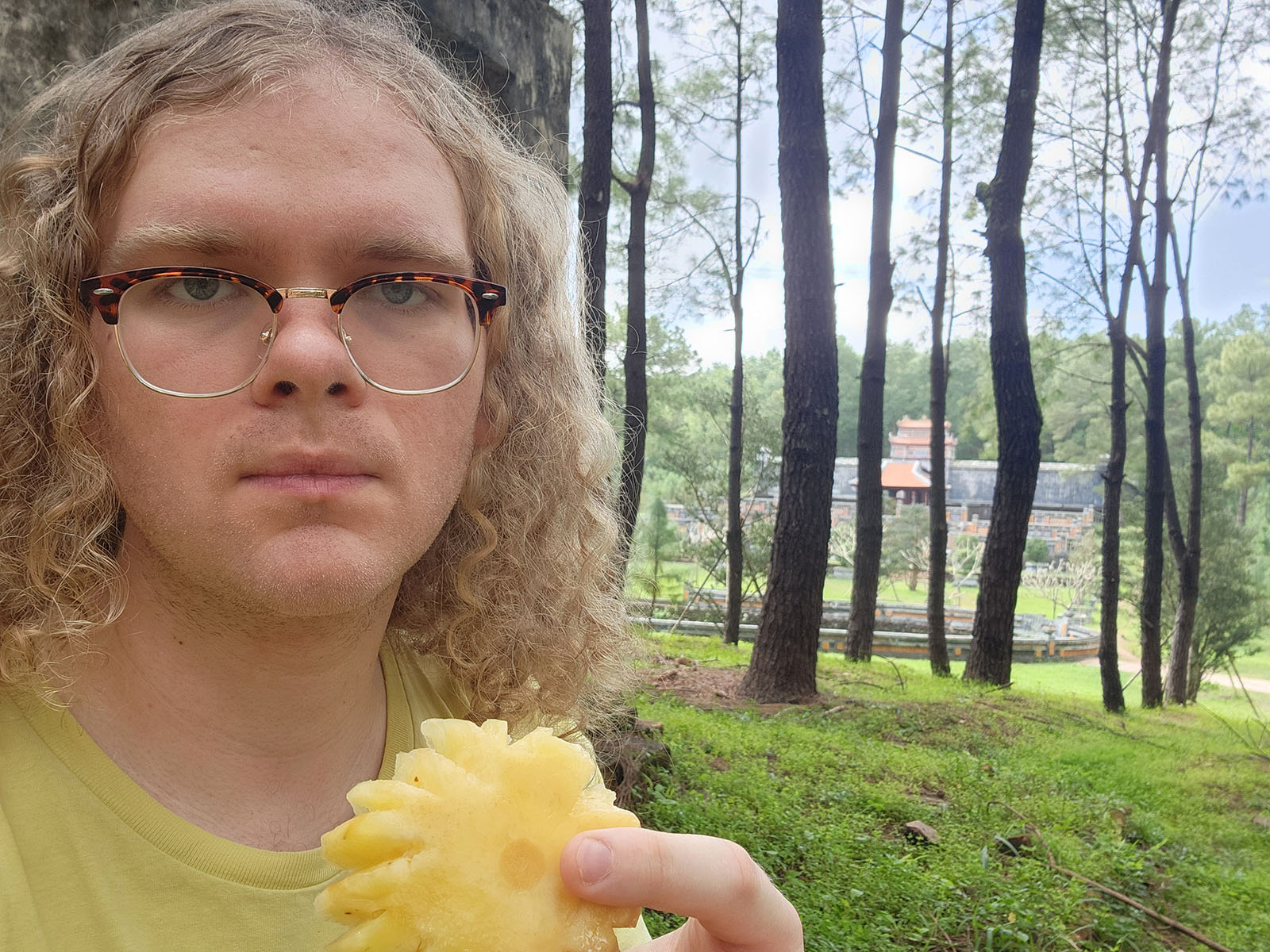 Damian's selfie surrounded by tall trees, through which a mausoleum complex can be seen.