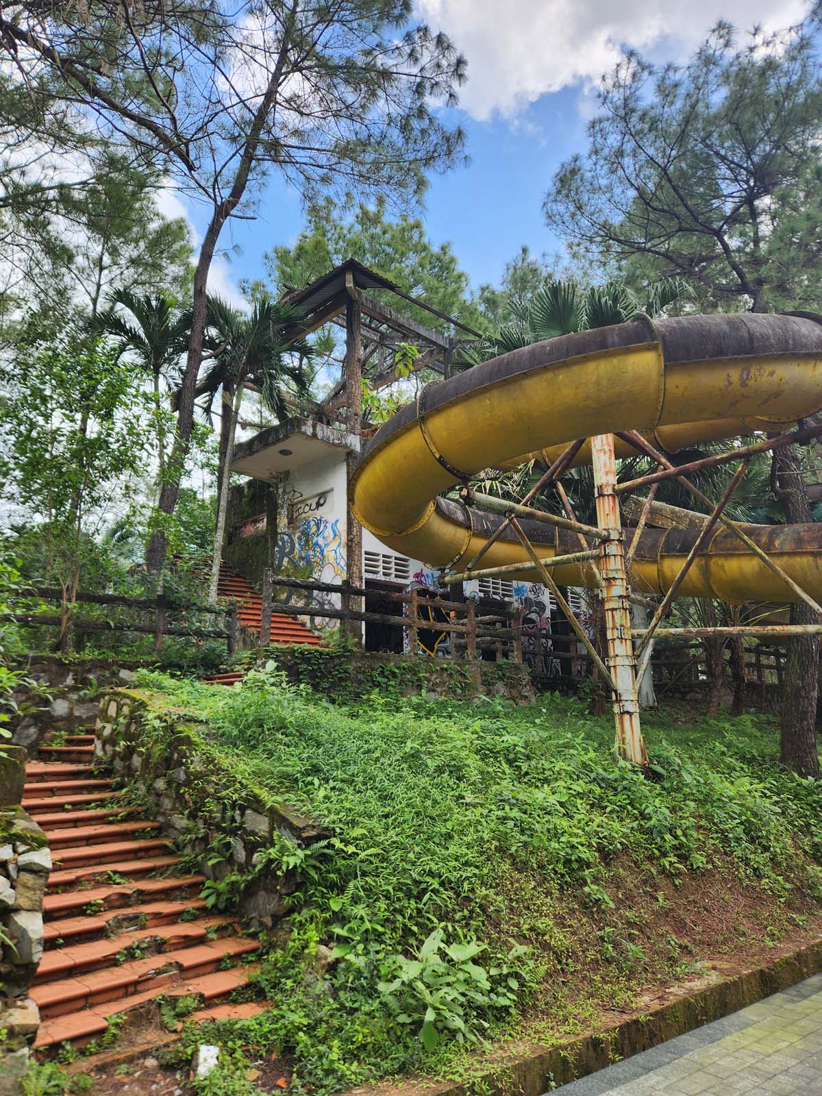 A photo looking up at an elevated boarding platform for three waterslides covered in green biofilm and lichen.