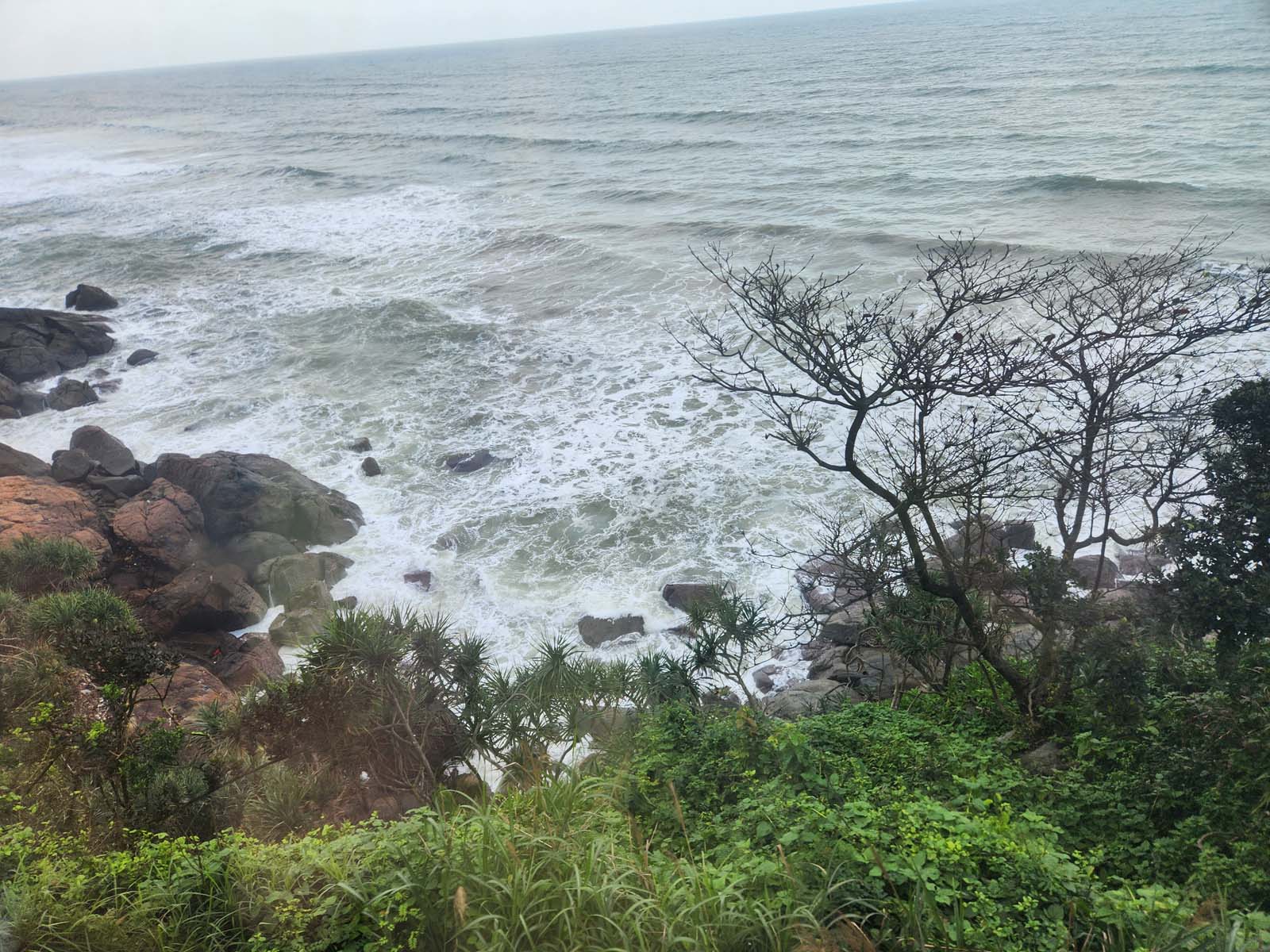 A photo of white, choppy waves against a rocky shore, seen from the train tracks above.
