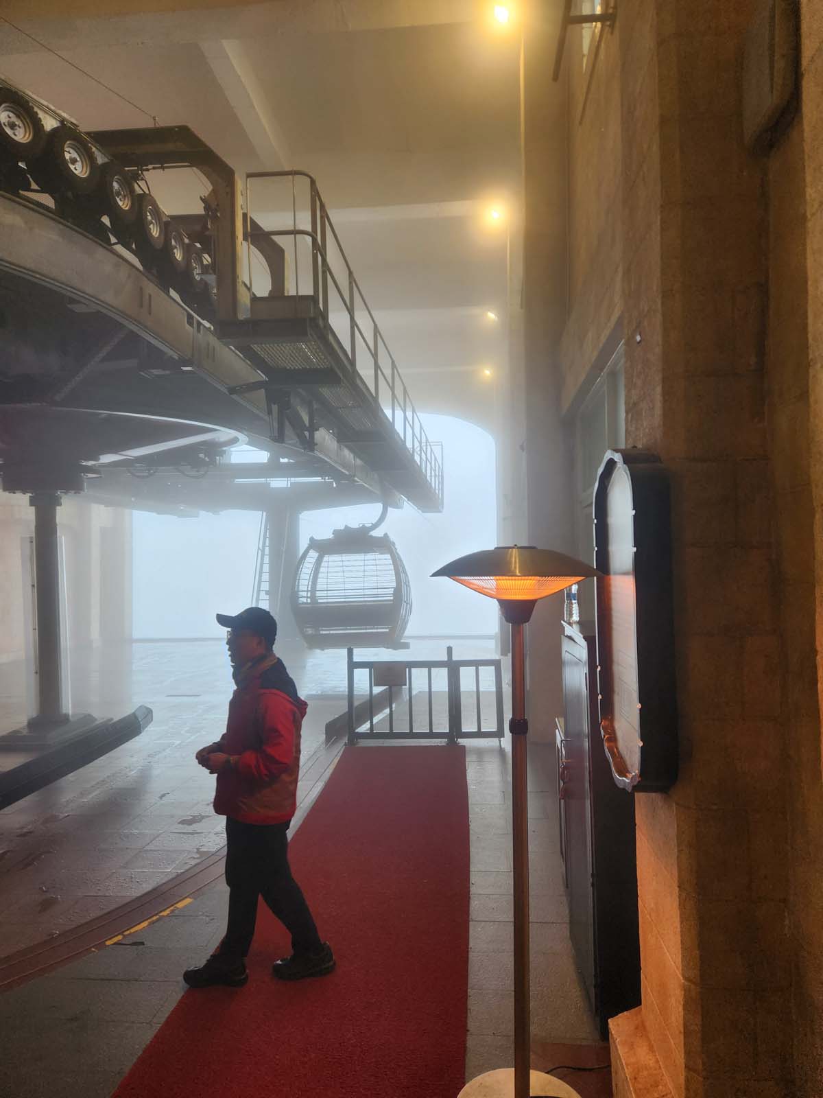 A cable car terminal. Nothing is visible outside of the small structure, and even inside, the fog limits visibility.