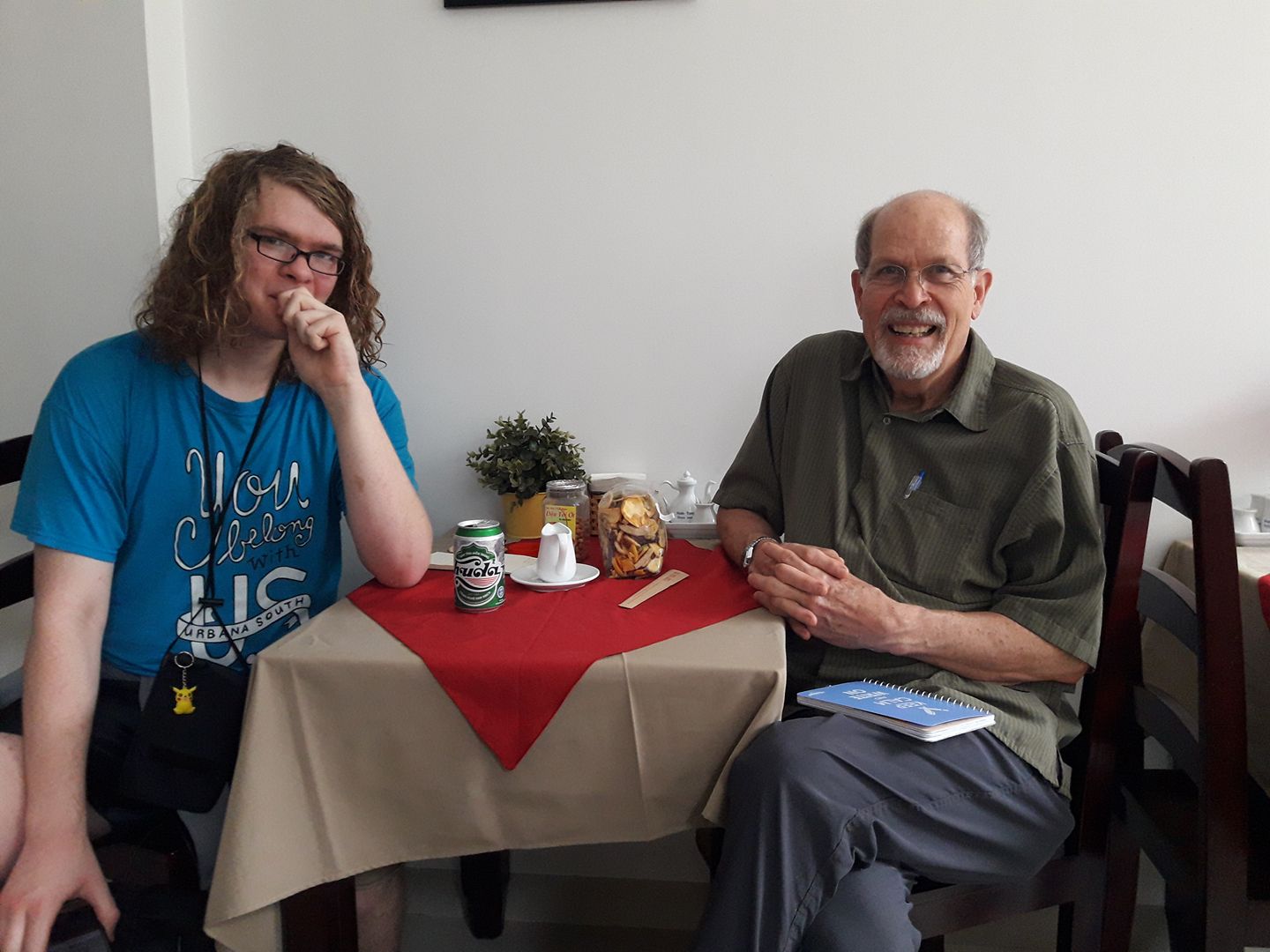 A photo from 2018 of Damian and Grandpa Mike eating breakfast. On the table is a green can of Huda brand beer. Grandpa smiles to the camera while Damian looks bashful.